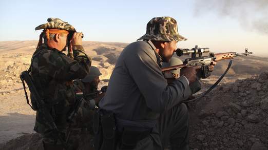 Iraqi Kurdish Peshmerga troops watch as smoke billows from the town of Makhmur